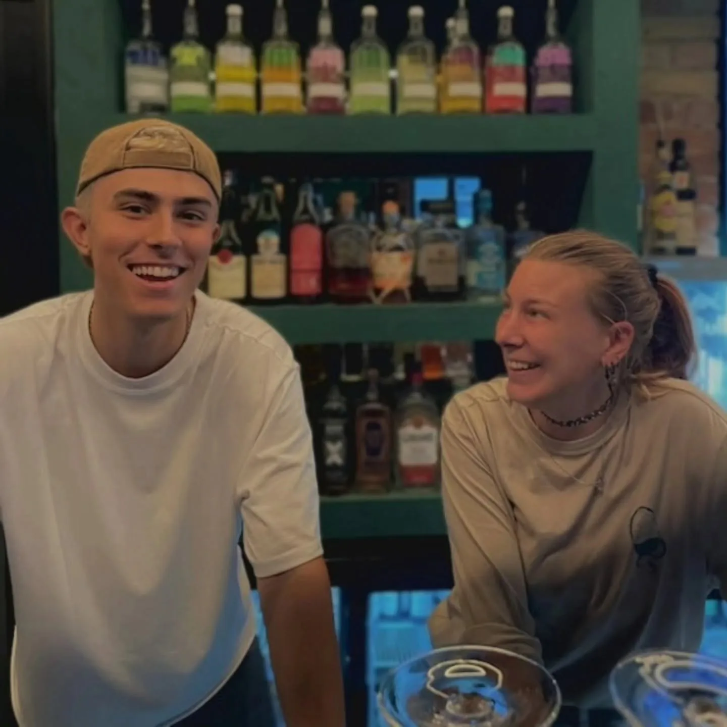 Två ur personalen skrattar bakom baren framför hyllor med flaskor